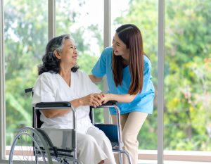 車椅子に座った高齢女性と、それに寄り添う若い女性の介護士が笑顔で会話している