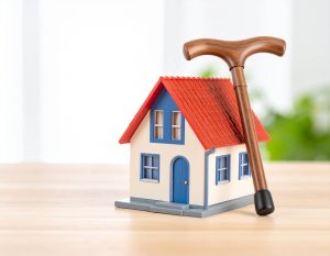 木製の家のミニチュアと高齢者用の杖が並んで置かれている